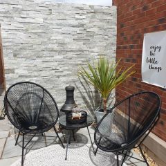 Ivory split face tiles on a patio feature wall with black contemporary metal chairs, wood burner and plant in pot
