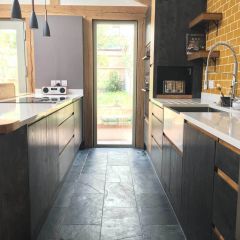Brushed black 600x300mm natural slate floor tiles pictured in a contemporary black wood kitchen with oak beams and yellow wall tiles