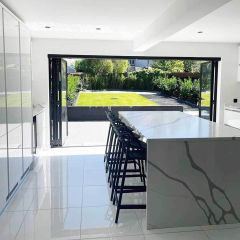 Super white polished porcelain floor tiles in a contemporary white kitchen with marble island, black bar stools and open bifold doors.