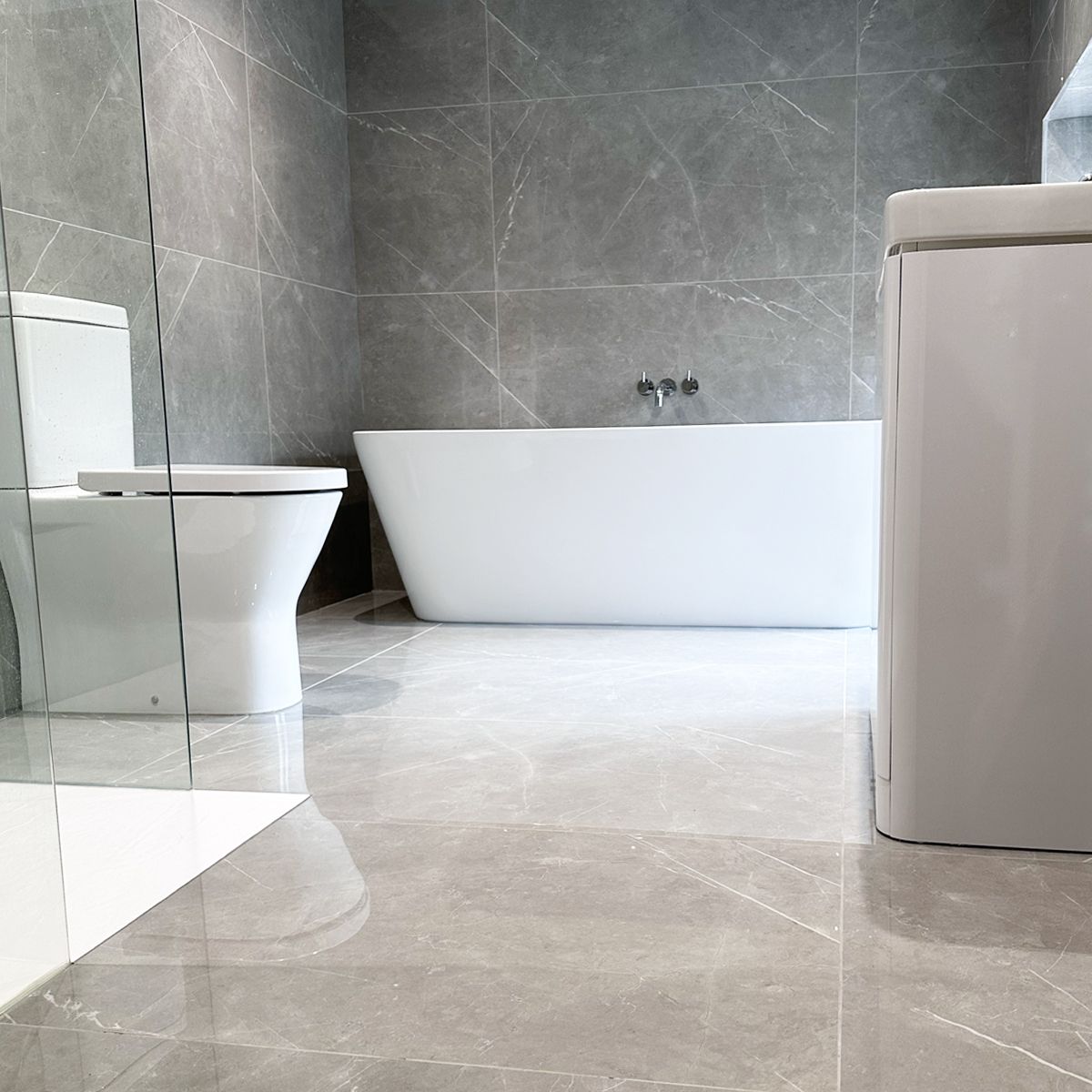 image of contemporary bathroom with soft grey large format marble effect wall and floor tiles, free standing bath, white basin, toilet and shower tray