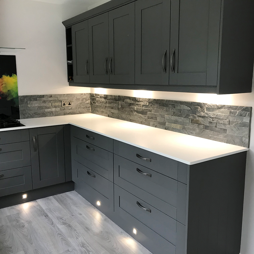 A wall in a kitchen covered in split face grey mosaic tiles. 